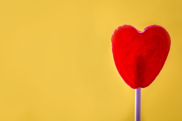 Czerwony lizak w kształcie serca na żółtej powierzchni Koncepcja miłości Walentynki.
