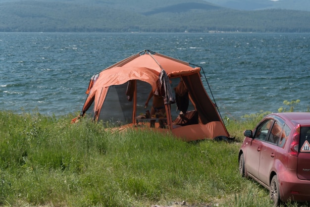 Zdjęcie czerwony namiot z siatką dla komarów stoi obok samochodu w lecie na brzegu jeziora