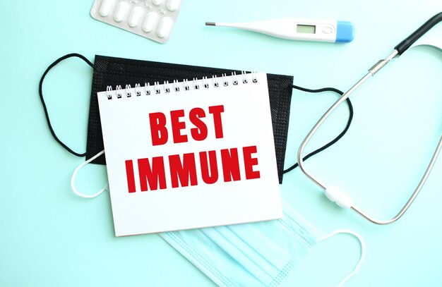 Czerwony napis BEST IMMUNE jest napisany w notatniku, który znajduje się na niebieskim tle obok materiałów medycznych