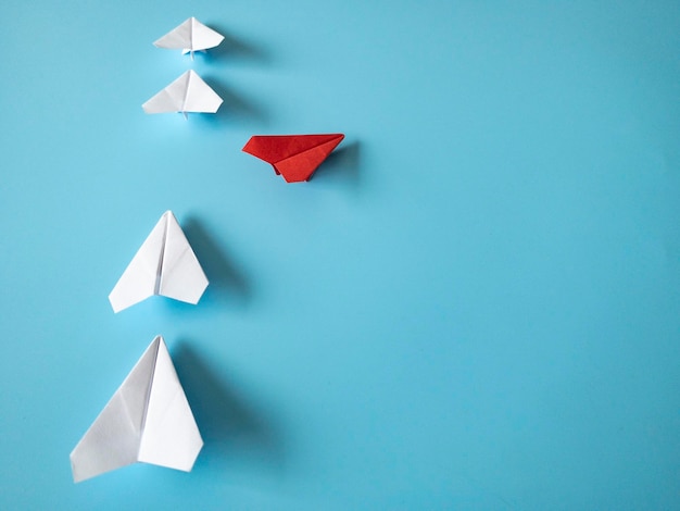 Czerwony papierowy samolot origami pozostawiając inne białe samoloty na niebieskim tle Skopiuj przestrzeń i koncepcję umiejętności przywódczych