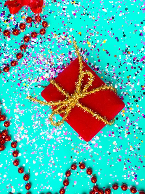 Czerwony prezent bożonarodzeniowy ze złotą kokardką na świątecznym tle zielonej mięty z konfetti Czerwone koraliki Świąteczna kartka pocztowa Koncepcja upominków rabatów sprzedaży