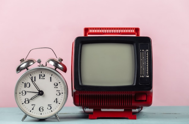 Czerwony retro stary przenośny mini telewizor i budzik na różowym tle.