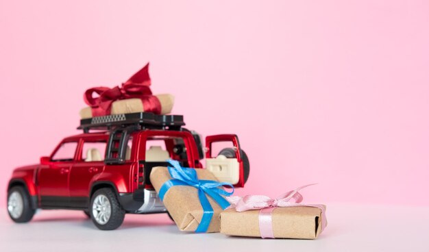 Zdjęcie czerwony samochodzik dostarczający pudełko prezentowe na różowym tle kopii przestrzeni