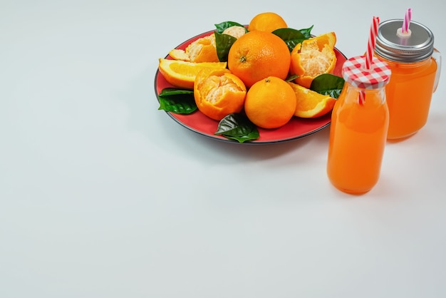 Czerwony talerz z pomarańczami i tangerines zielonymi liśćmi butelkuje z sokiem na lekkim tle