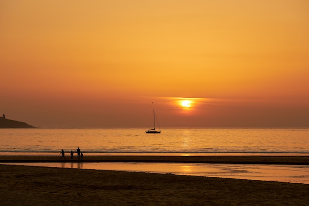 Czerwony zachód słońca z ludźmi spacerującymi na plaży Playa America w Galicji, Hiszpania.