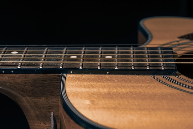 Część gitary akustycznej, gryf gitarowy ze smyczkami na czarnym tle.