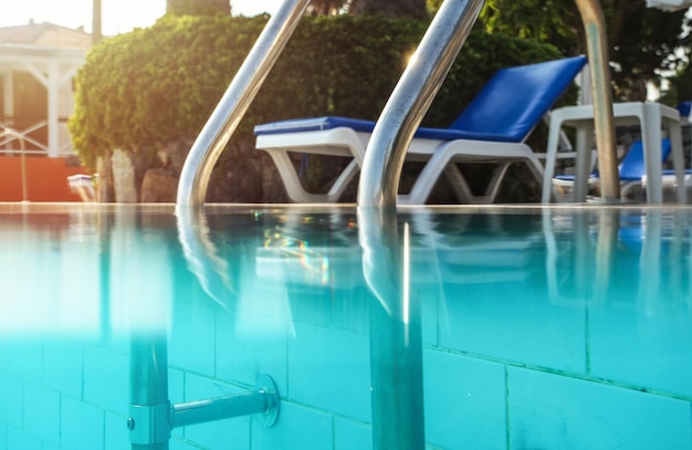 Częściowo podwodne zdjęcie, stalowe poręcze przy wejściu na basen, podświetlone słońce w tle. Obraz wakacje / relaks.
