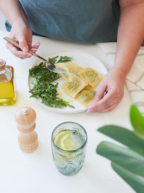 Częściowy widok dorosłej kobiety przy stole z widelcem w ręku, biorąc makaron ravioli