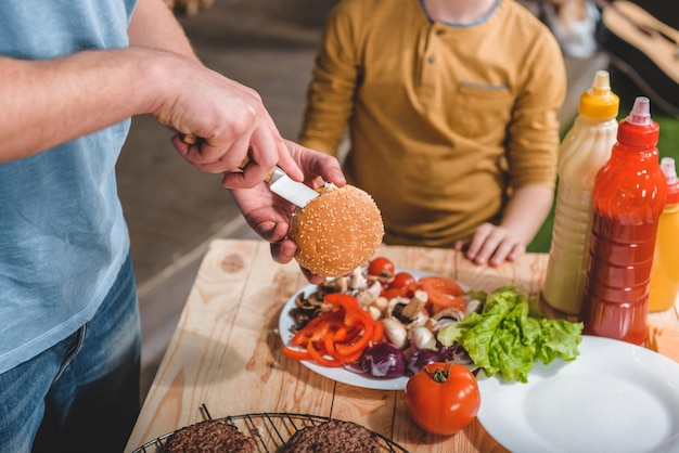 Zdjęcie częściowy widok taty i syna, którzy razem gotują hamburgery mięsne