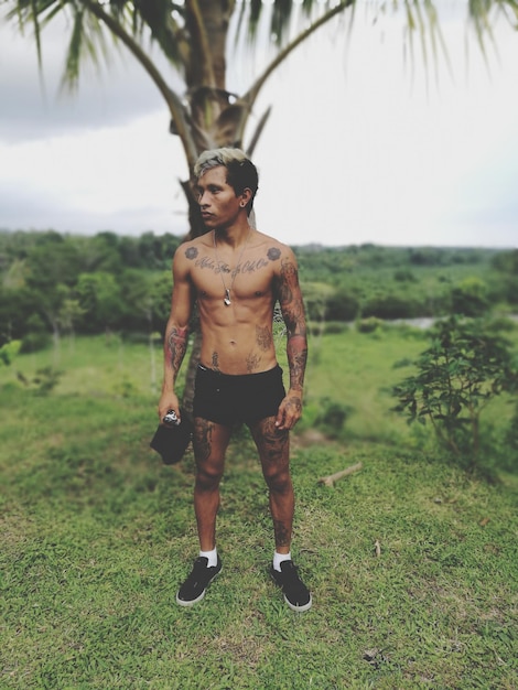 Człowiek bez koszuli z tatuażem stojący na drzewie na polu
