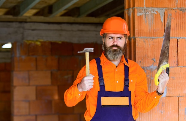 Człowiek Budowniczy W Niedokończonym Budynku Profesjonalny Mechanik Używa Piły I Młotka Do Budowy I Budowy Wykwalifikowany Architekt Naprawa I Naprawa Kariery Inżyniera Dojrzały Brodaty Mężczyzna W Kasku