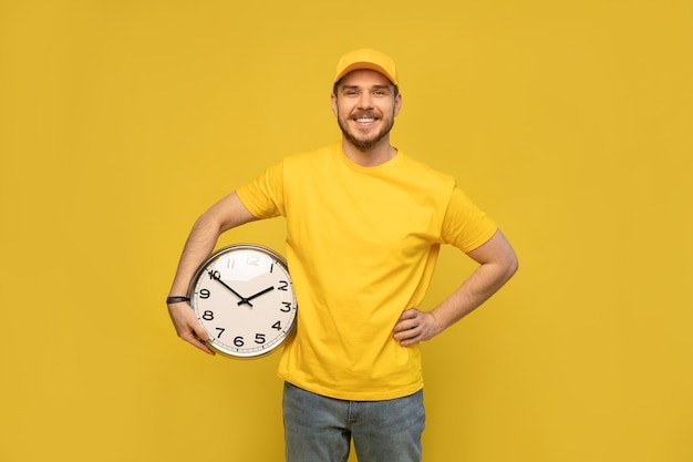 Człowiek Dostawy W żółtej Odzieży Roboczej Trzymać Zegar Na Białym Tle Na żółtej ścianie Portret Studyjny