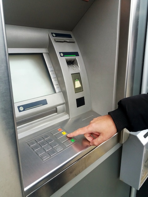 Człowiek korzysta z bankomatu za pomocą kart płatniczych i wprowadza kod PIN / pass na klawiaturze numerycznej.