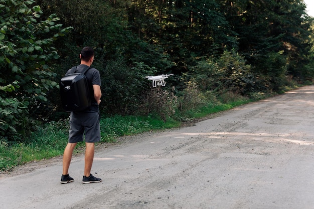 Człowiek latający dronem w drodze. Młody mężczyzna nawigujący latającym dronem