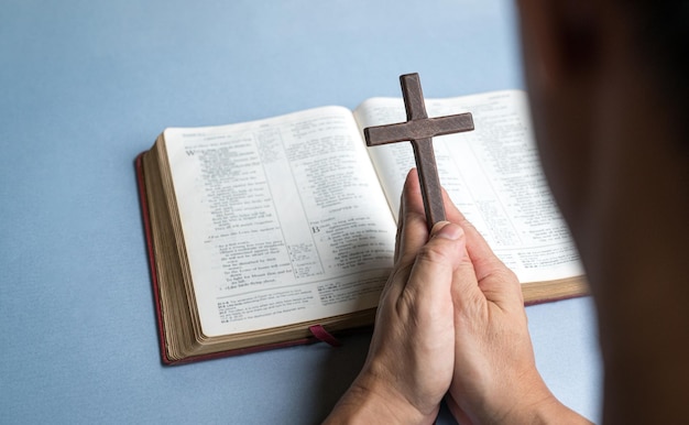 Człowiek modlący się trzymając krzyż krucyfiks z otwartą Biblią w tle