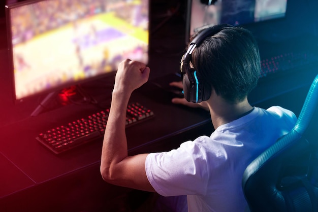 Człowiek na ekranie komputera i podekscytowany gracz z słuchawkami świętowanie i osiągnięcia e-sportów z tyłu twórca treści influencer lub streamer z zestawem słuchawkowym do gry wideo online lub nocy w domu