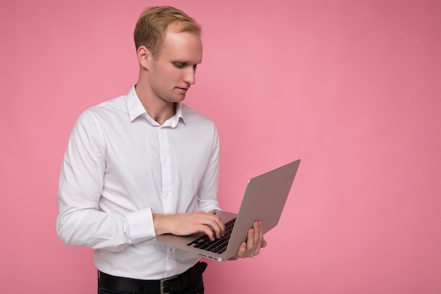 Człowiek Posiadający Komputer Laptop Wpisując Na Klawiaturze Na Sobie Białą Koszulę Patrząc Na Monitor Na Białym Tle Nad Różową ścianą.