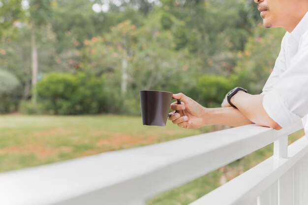 Człowiek relaxjng ręka trzyma kubek kawy stojąc na balkonie.