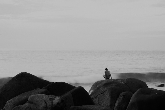 Zdjęcie człowiek siedzący na skale patrzący na morze na tle nieba