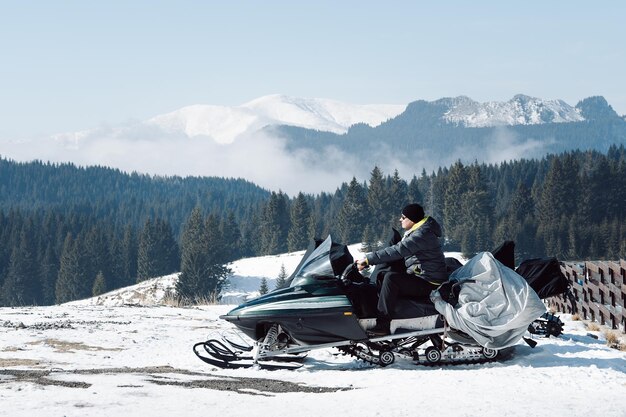 Człowiek siedzący na skuterze śnieżnym przed śnieżnymi górami na tle nieba