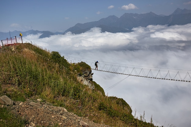 Człowiek spaceru na moście wiszącym i patrząc na zachmurzone góry poniżej.