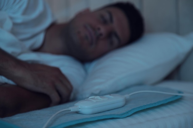 Człowiek śpiący w łóżku z elektryczną podkładką grzewczą koncentruje się na kablu