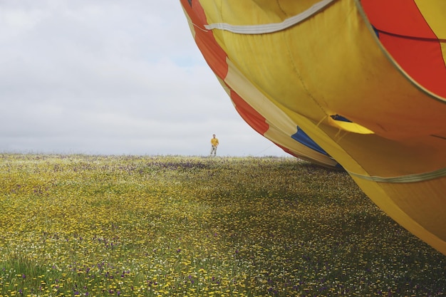 Zdjęcie człowiek stojący przy balonie na gorącym powietrzu na lądzie przeciwko niebu
