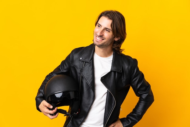 Człowiek w kasku motocyklowym na białym tle na żółtym tle, patrząc z boku i uśmiechnięty