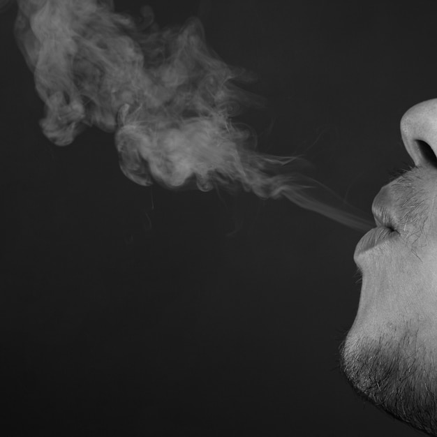 Zdjęcie człowiek wydycha dym papierosowy z bliska, monochromatyczny