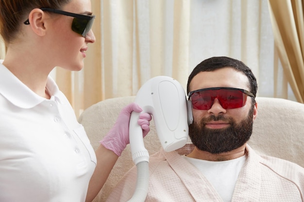 Człowiek z brodą otrzymuje laserową terapię twarzy od profesjonalnego kosmetologa w klinice piękności