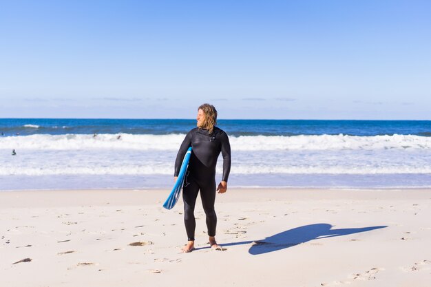 człowiek z deski surfingowej na brzegu oceanu. Surfer w mokrym kostiumie