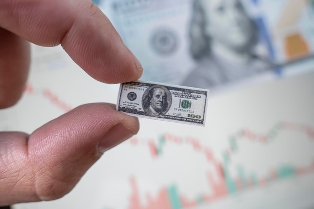 Człowiek z inflacją dolara trzyma mały banknot sto dolarów na tle spadającego wykresu na giełdzie Niskie dochody z handlu na giełdzie Upadłość