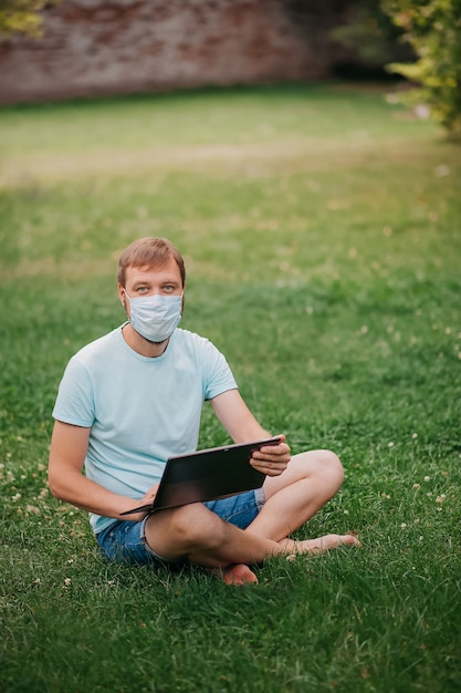 Człowiek z maską ochronną za pomocą laptopa w naturze