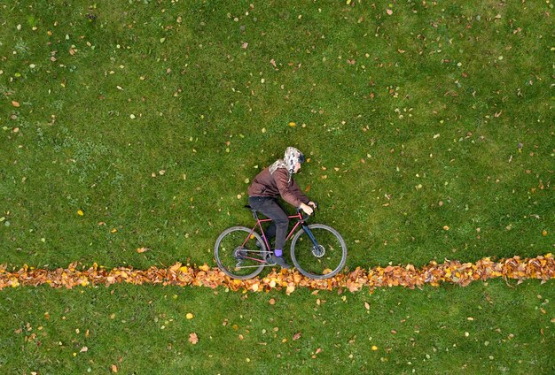 Człowiek z rowerem leży na zielonej trawie z jesiennymi liśćmi. Kreatywna modna jesień koncepcja.