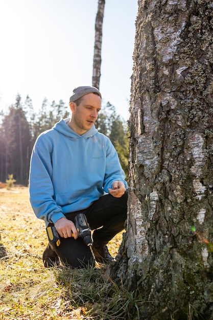 Człowiek zbierający sok z brzozy w spokojnym lesie, zaangażowany w zrównoważoną praktykę pozyskiwania z drzew naturalnych źródeł wody