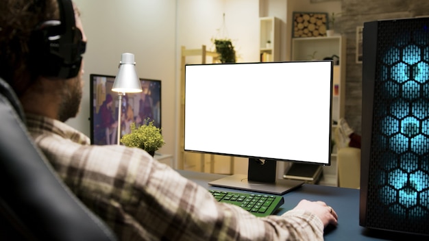 Człowiek ze słuchawkami, grając w gry na komputerze z zielonym ekranem w salonie.