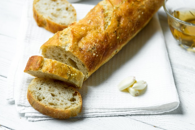 Czosnku bagietka na białym kuchennym ręczniku na drewnianym stole.