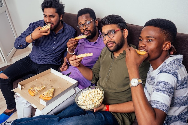 czterech Afroamerykanów jedzących pizzę na imprezie domowej, rzucających w siebie popcornem.