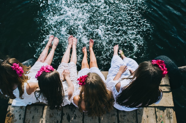 Czterech przyjaciół młodych dziewcząt siedzi na jet z nogami wiszące do wody w letni dzień