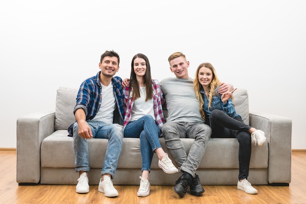Czterech szczęśliwych przyjaciół siedzi na kanapie na białym tle ściany