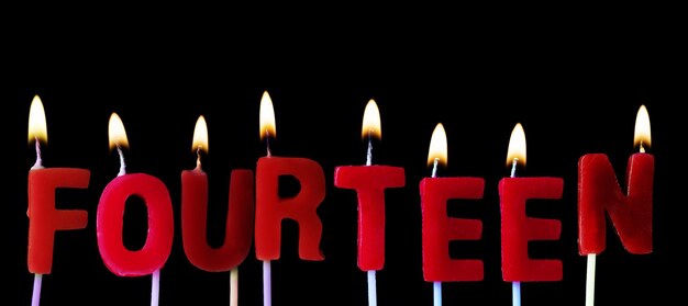Zdjęcie czternaście napisanych czerwonymi urodzinowymi świeczkami na czarnym tle
