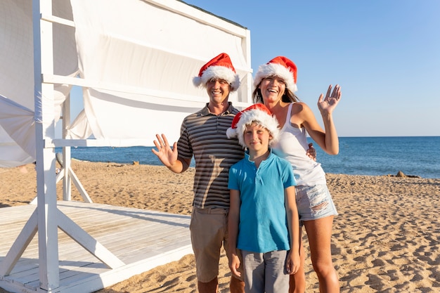 Czteroosobowa rodzina, mama tata i dwoje dzieci w czapkach Świętego Mikołaja na piaszczystej plaży. Wesołych Świąt Bożego Narodzenia rodzina świętuje nowy rok nad brzegiem morza.