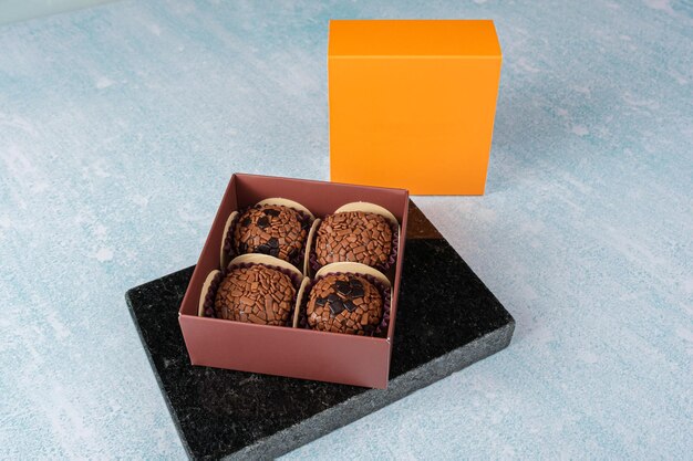 Cztery brygadeiros w pudełku na marmurowym kamieniu W pobliżu znajduje się pomarańczowe wieczko pudełka
