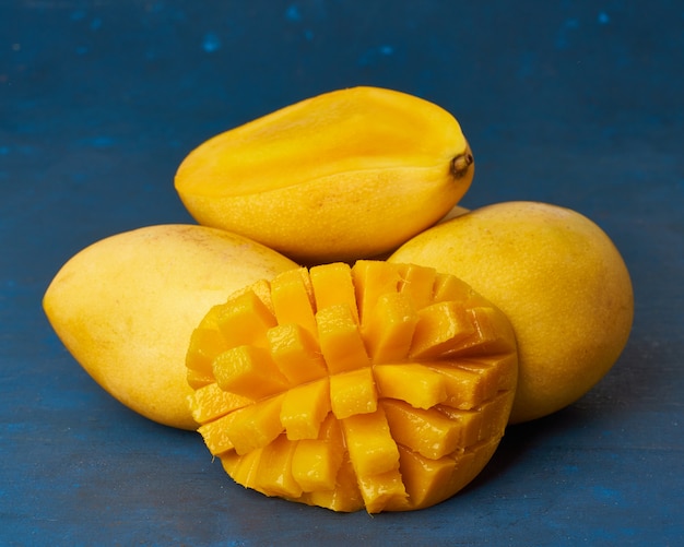 Cztery Całe Owoce Mango Na Granatowym Stole I Pokrojone W Plasterki. Duże Soczyste Dojrzałe żółte Owoce