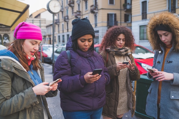 Cztery młode kobiety używa smartphone