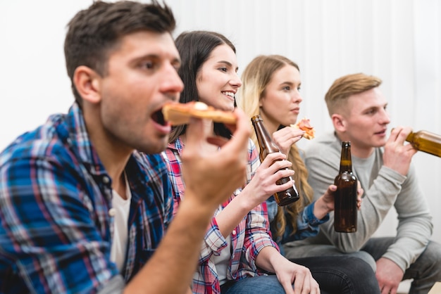 Cztery osoby na kanapie jedzą pizzę i piją piwo na białym tle