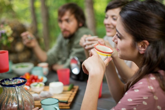 Cztery osoby siedzące wokół drewnianego stołu na zewnątrz w lesie, dzielące posiłek