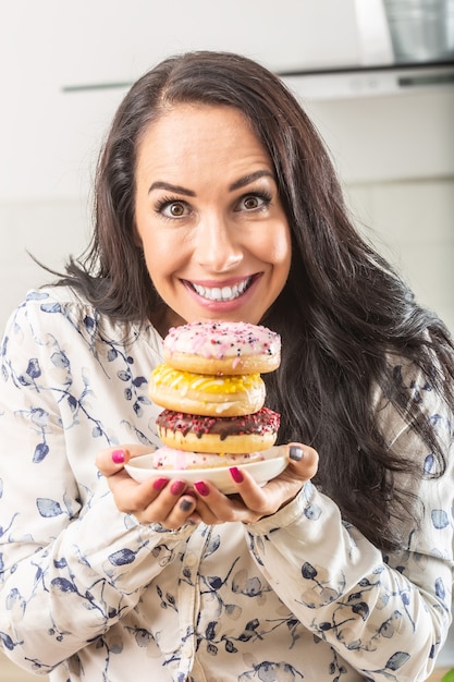 Cztery pączki na talerzu trzymanym przez ładną brunetkę.