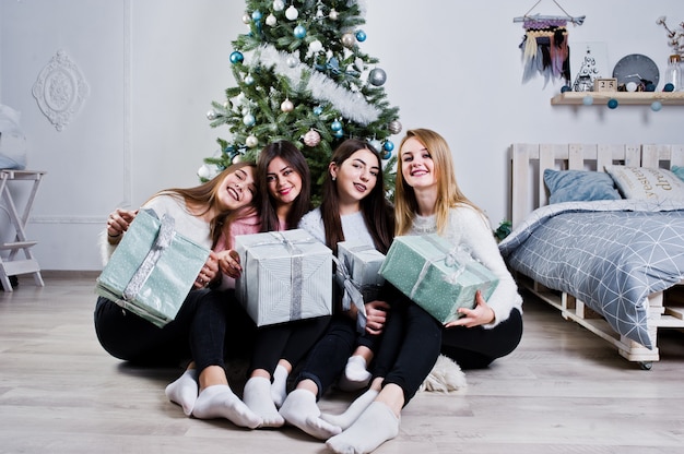 Cztery śliczne przyjaciele dziewczyny noszą ciepłe swetry, czarne spodnie na tle choinki z dekoracją świąteczną w białym pokoju.