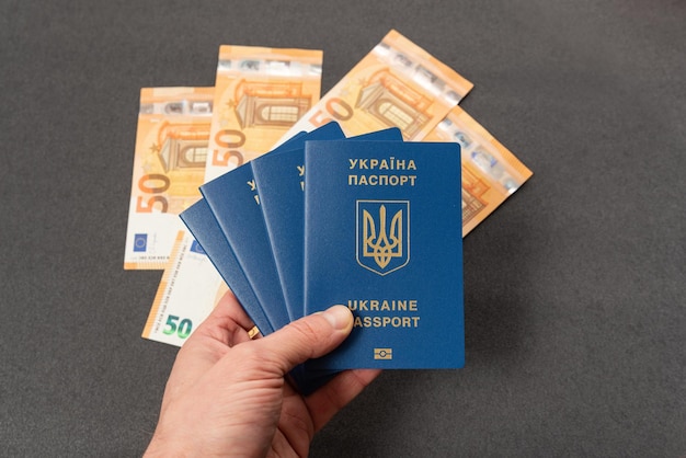 Cztery ukraińskie paszporty w gotówce w męskiej dłoni euro na tle Uzyskanie i wymiana zagranicznego paszportu Podróż za granicę